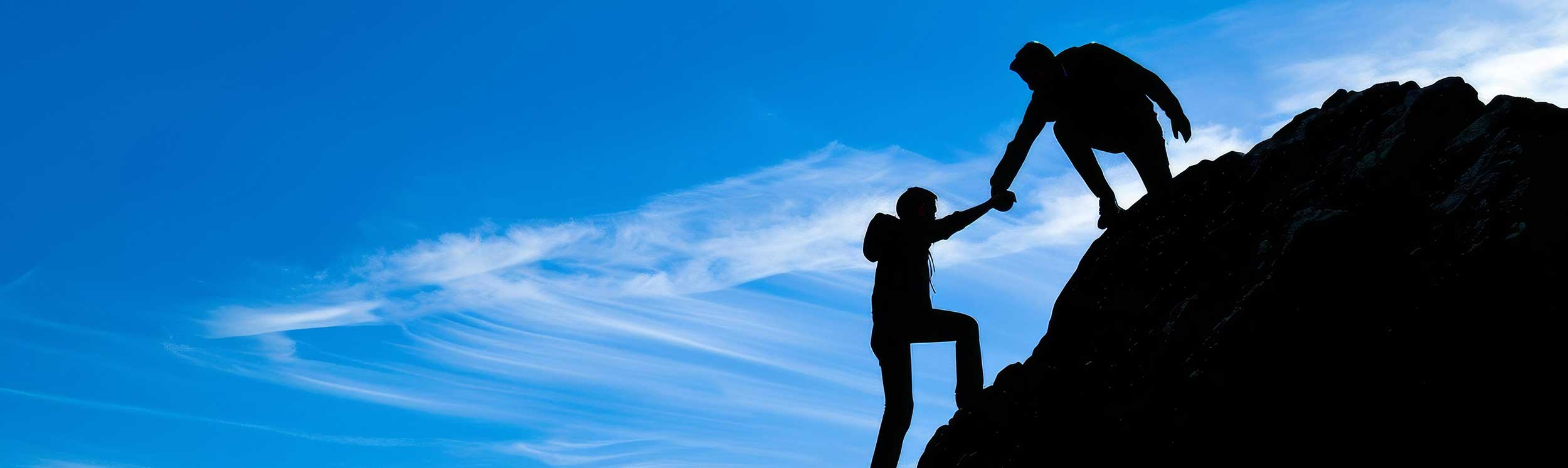 Zwei Personen helfen sich beim Aufstieg auf einen Berg als Symbol für Zusammenarbeit, Unterstützung und gemeinsames Wachstum im Executive Mentoring.