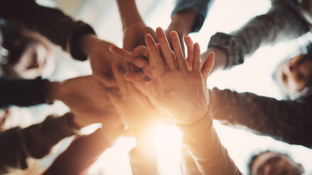 Führung im Wandel: Ein Team legt gemeinsam die Hände übereinander und steht für Zusammenhalt, Vertrauen und gemeinsames Handeln.